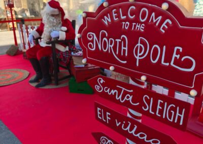 Cartel navideño que indica 'Welcome to the North Pole' con direcciones a Santa Sleigh, Elf Village y Reindeer Way.