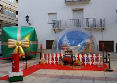 Decoración navideña con bola de nieve gigante, regalo inflable y buzón para cartas en una plaza.