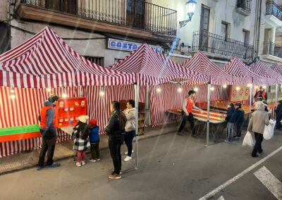 Puestos de feria con carpas de rayas rojas y blancas en una calle iluminada.