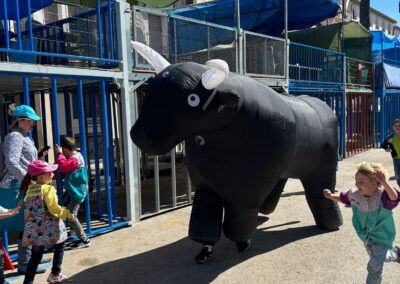 Niños corriendo junto a un toro hinchable en un encierro infantil al aire libre.