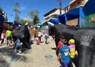 Niños interactuando con toros hinchables en un encierro infantil al aire libre.