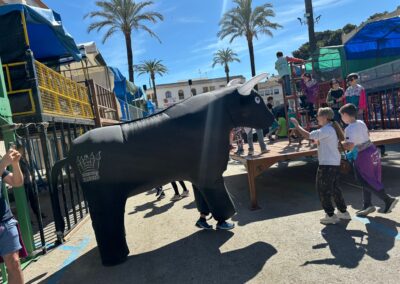 Niños participando en un encierro infantil con toro hinchable al aire libre.