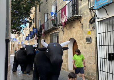 Niño corriendo frente a toros hinchables en un encierro infantil por una calle estrecha.