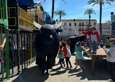 Toros hinchables en un encierro infantil con niños jugando alrededor.